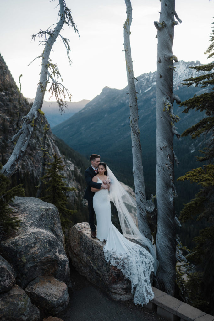 A couple standing on a rock, with mountains behind them during their North Cascades National Park elopement.