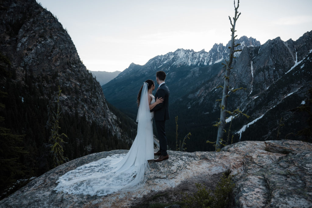 A couple standing on a rock, with mountains behind them during their North Cascades National Park elopement