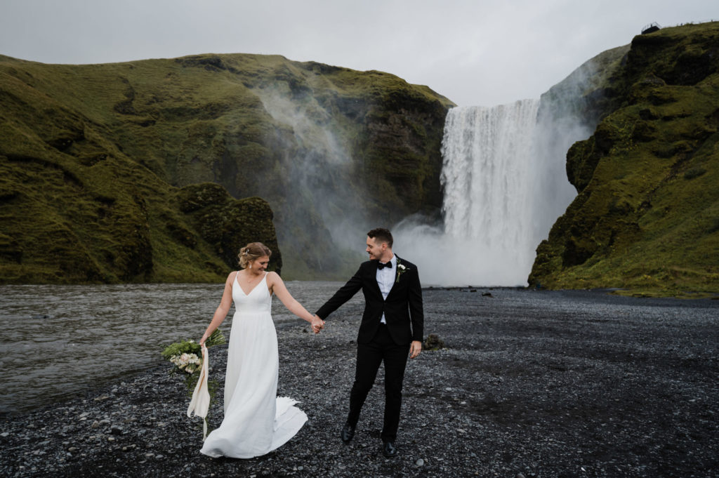 A couple who decided to elope in Iceland is standing in front of Skogafoss.