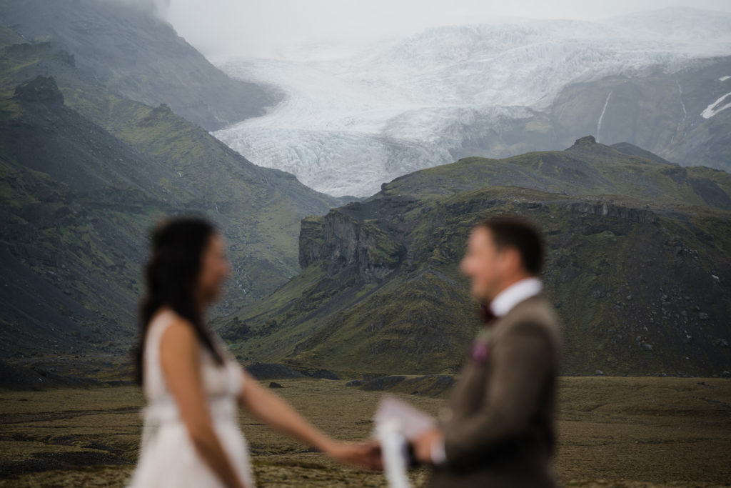 A couple who decided to elope in Iceland is standing in front of a glacier during their ceremony.