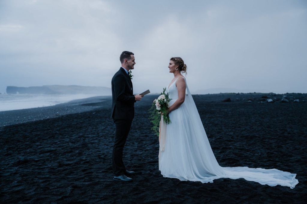 A couple is facing each other during their elopement ceremony on a black sand beach in Iceland.