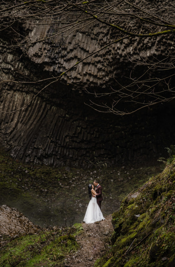 A couple ready to elope in Oregon, standing at the base of a waterfall.