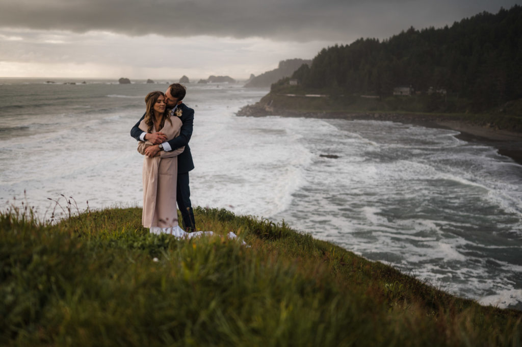 A couple standing on a cliff over the ocean, at one of the best places to elope in Oregon!
