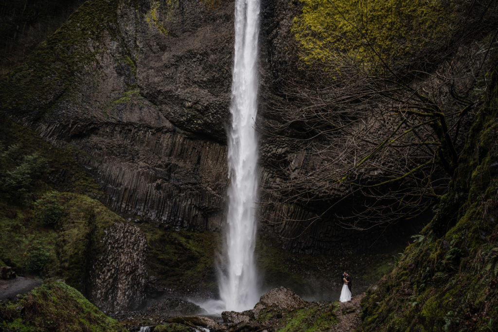 A couple standing at the base of a waterfall as they elope in oregon.