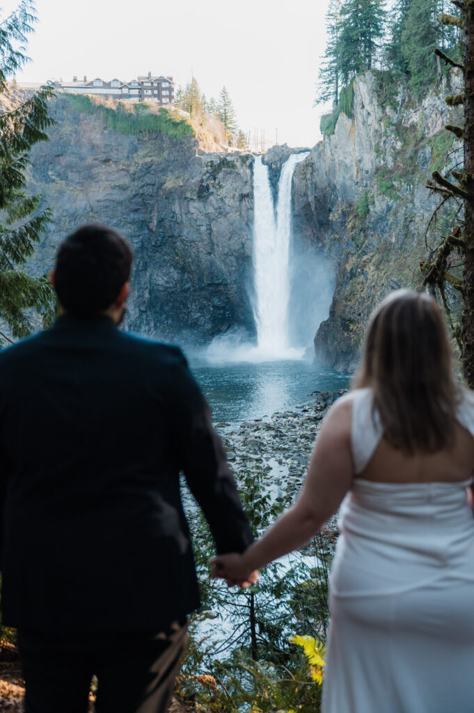 Bride and groom holding hands and looking out at Snoqualmie Falls in Washington State