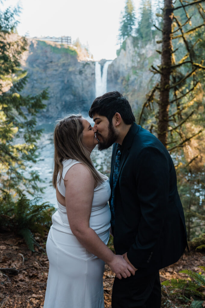 Newly married couple sharing their first kiss in front of Snoqualmie Falls