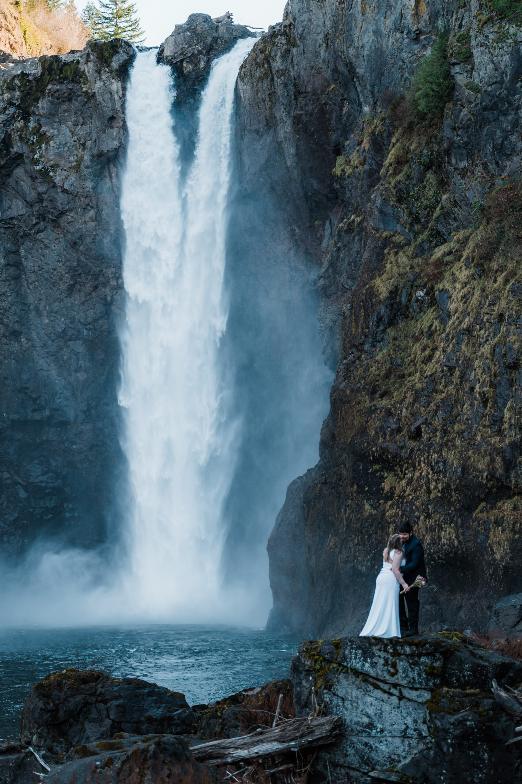 Bride and groom standing next to Snoqualmie Falls on their elopement day in Washington