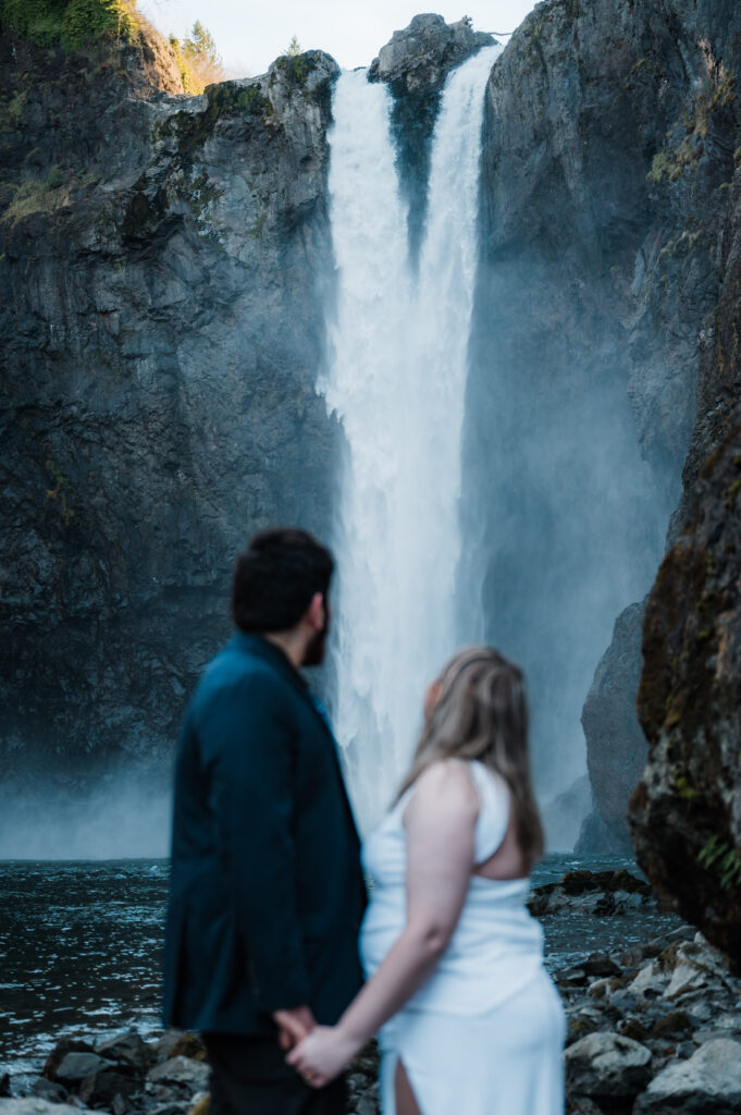 Couple holding hands in front of Snoqualmie Falls on their elopement day