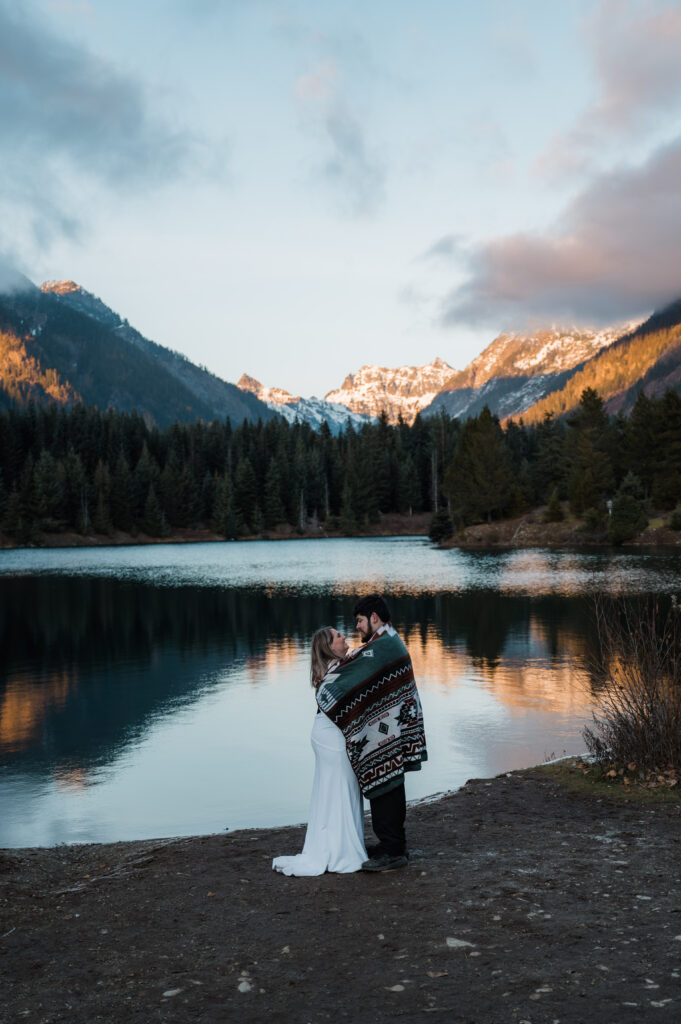 Couple cozied up under a blanket while watching the sunset at Gold Creek Pond on their elopement day in Washington