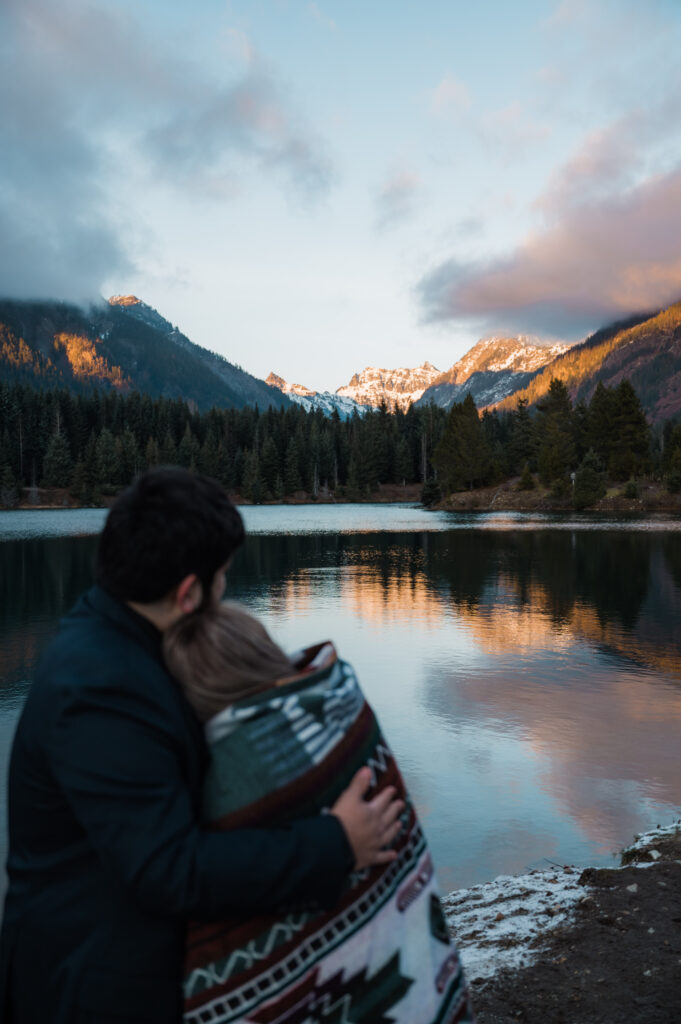 Couple cozied up under a blanket while watching the sunset over the mountains at Gold Creek Pond in Washington State