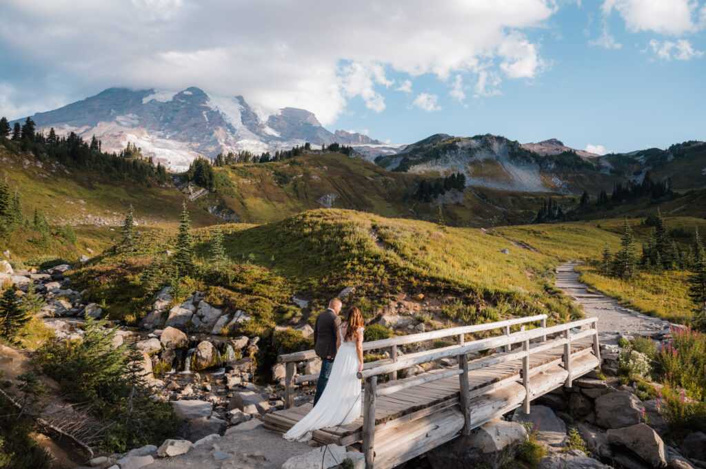 Bride and groom walking across a bridge at Myrtle Falls with views of Mount Rainier in the background 