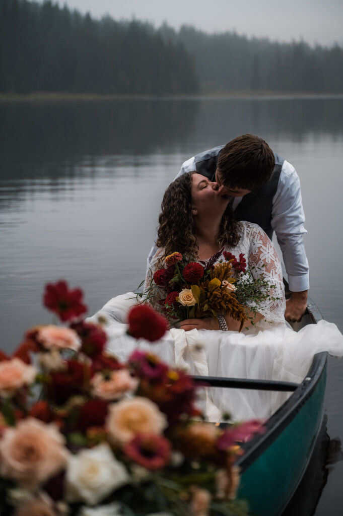 Couple kissing in a canoe during their elopement day at Trillium Lake near Mount Hood, Oregon while holding fall florals