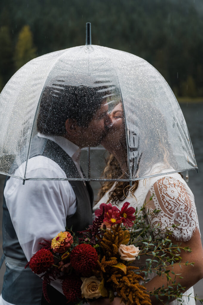 bride and groom kissing under an umbrella in the rain during their elopement day at Trillium Lake near Mount Hood Oregon
