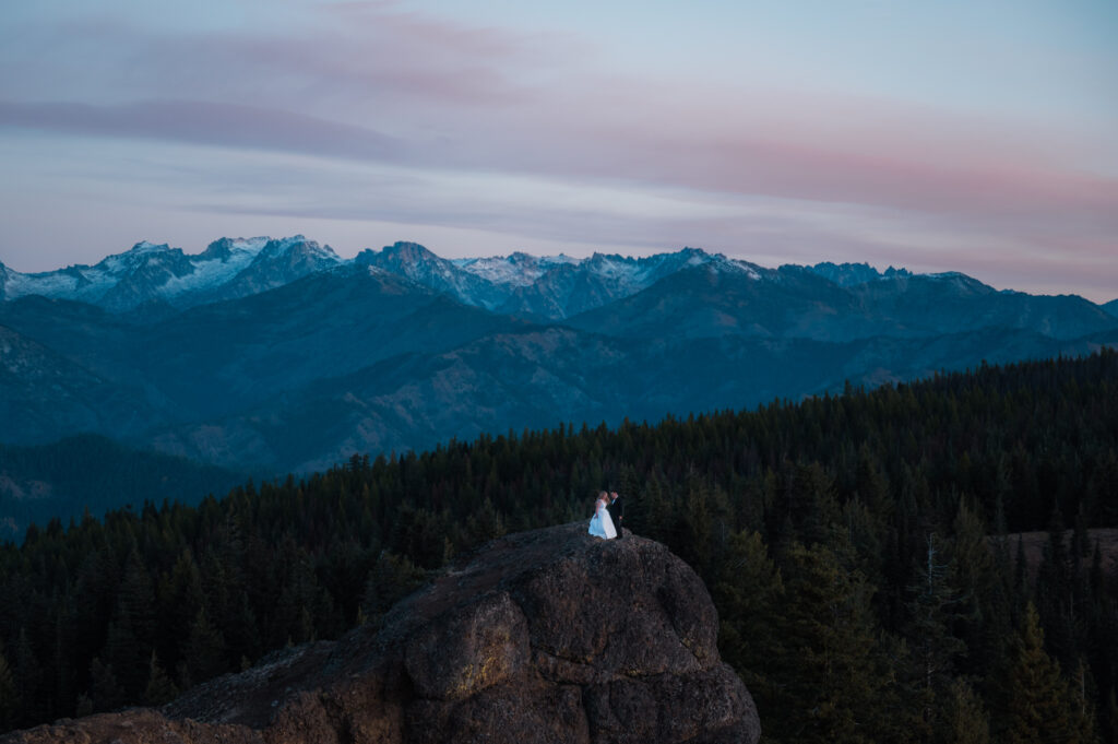 Eloping couple standing on a cliff surrounded by mountain views at Red Top Fire Lookout in Washington State