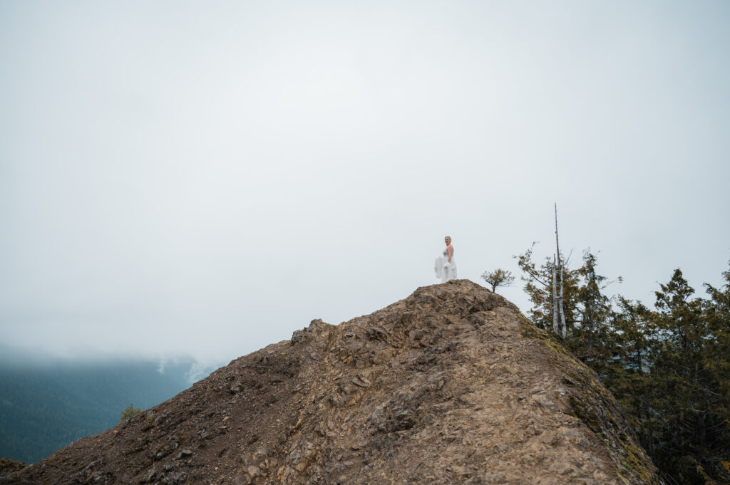 bride standing on top of Mount Storm King with moody clouds in the background