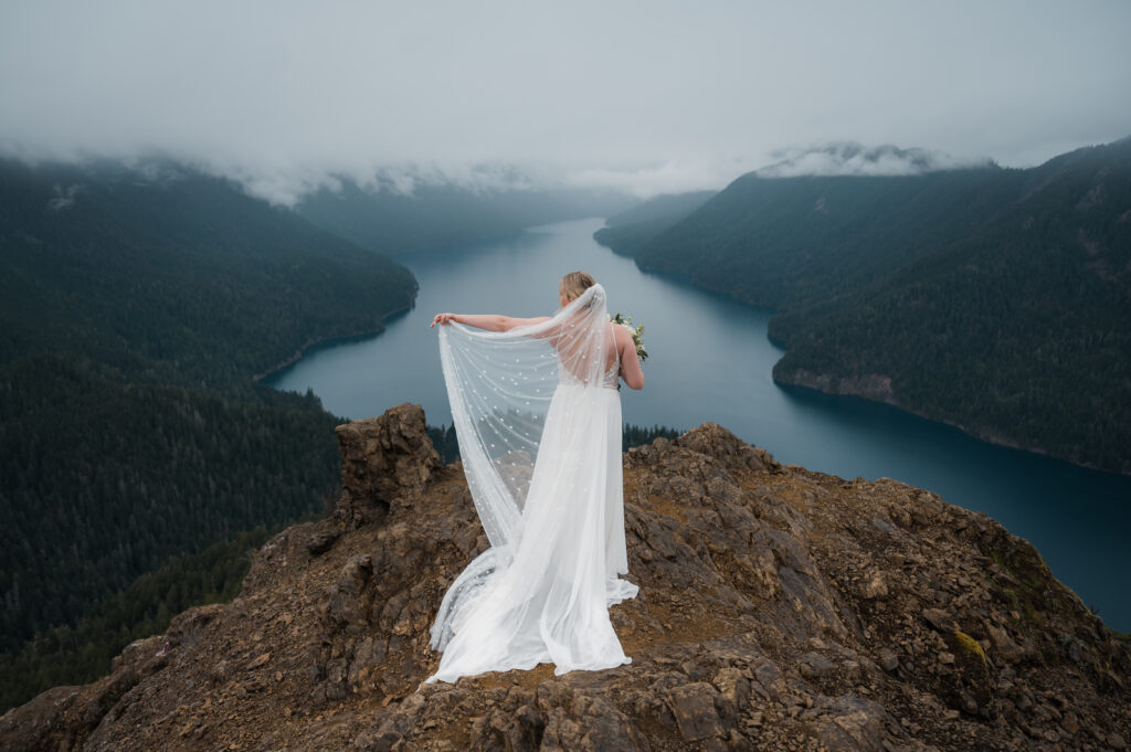 bride with a veil posing for photos in front of Lake Crescent and the mountains during her hiking elopement in Olympic National Park