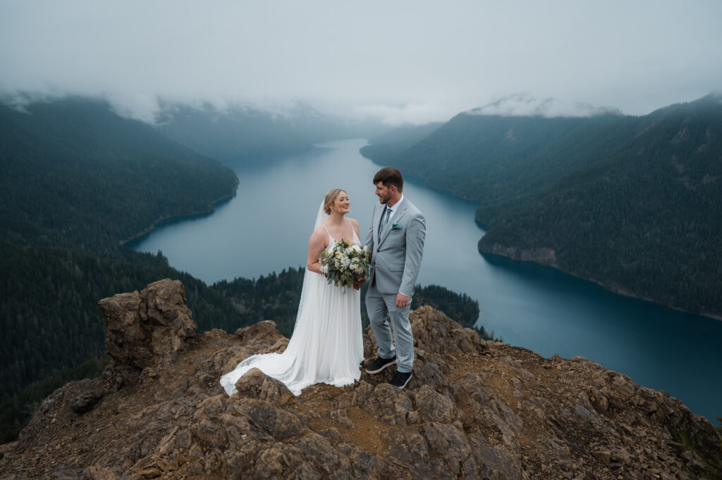 eloping couple standing at the top of Mount Storm King with views of the mountains and Lake Crescent in the background