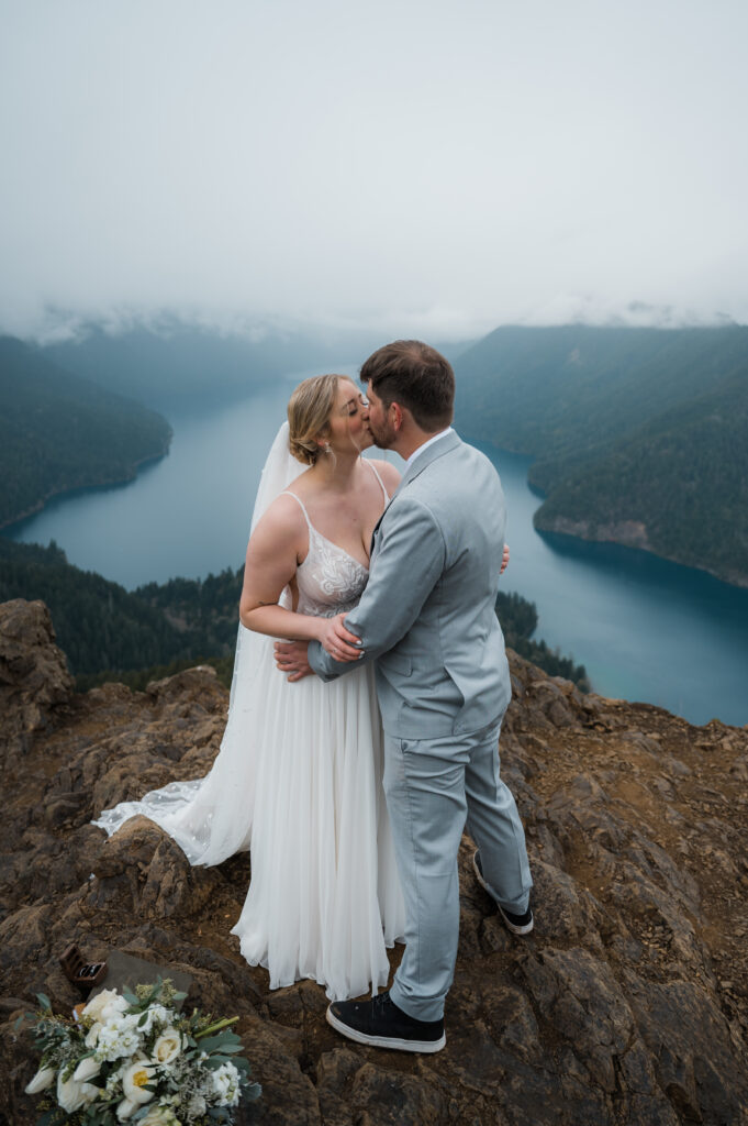 bride and groom share their first kiss during their hiking elopement to the top of Mount Storm King in Olympic National Park with views of the mountains and Lake Crescent in the backgrond