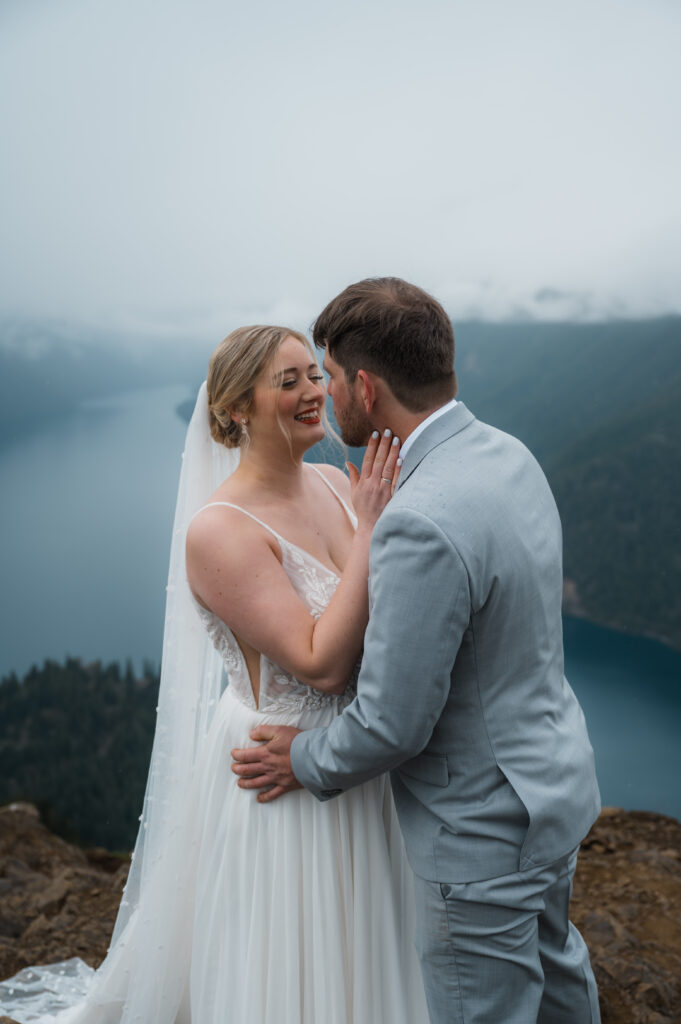 bride and groom standing on top of Mount Storm King with views of the mountains and Lake Crescent in Olympic National Park