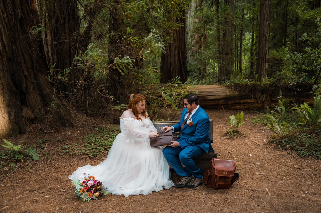 Bride and groom sit on a wood bench in Jedediah Smith Redwoods and read letters from family