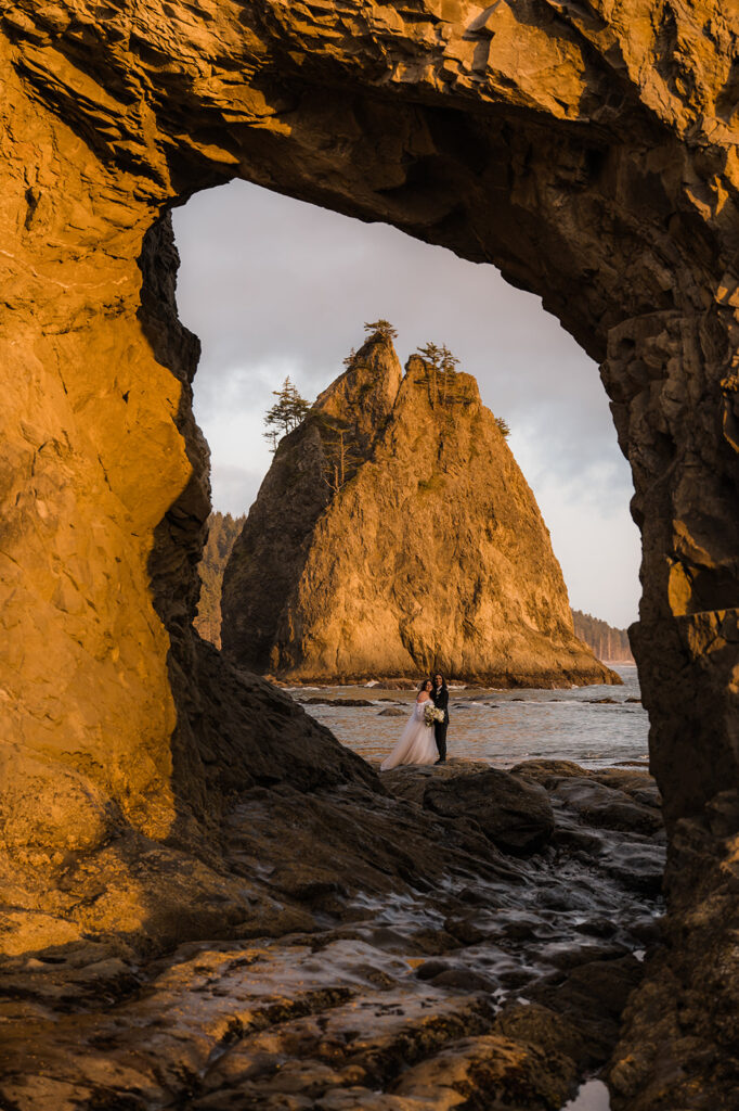 Bride and groom take a picture in the hole in the wall at rialto beach