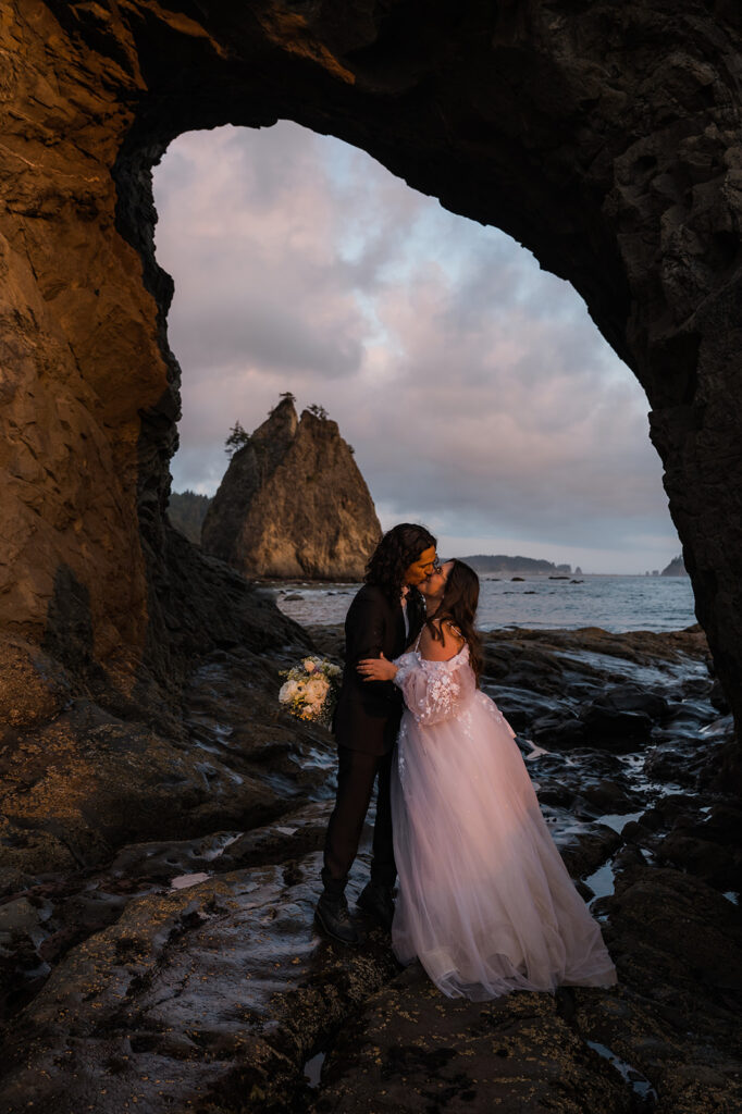 Bride and groom take a picture in the hole in the wall at rialto beach