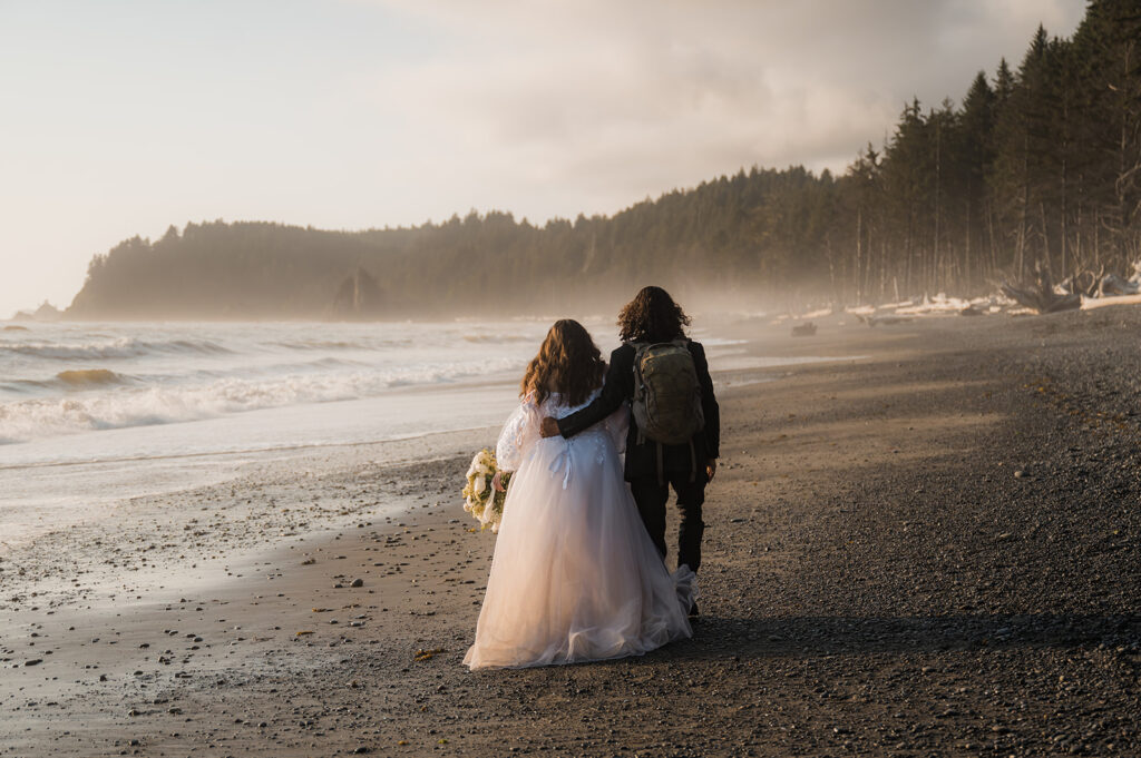 Bride and groom walk along the shore of Rialto Beach with fog in the distance