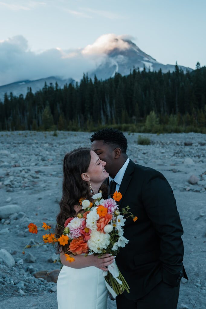 Bride and groom take couples portraits with Mt. Hood peaking through the clouds in the backdrop