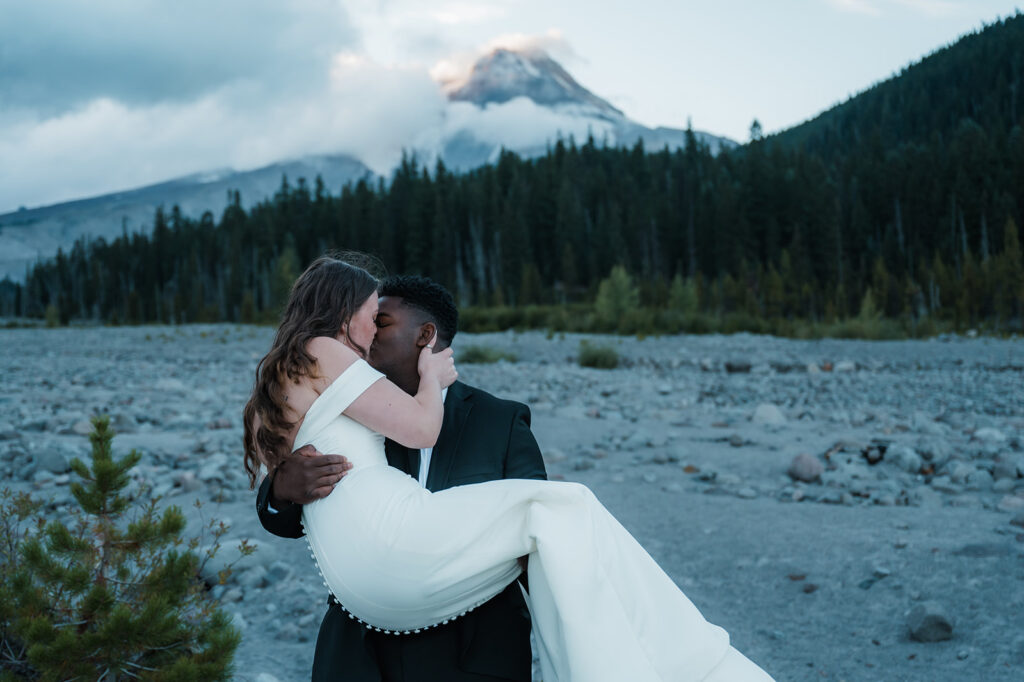 Bride and groom take couples portraits with Mt. Hood peaking through the clouds in the backdrop