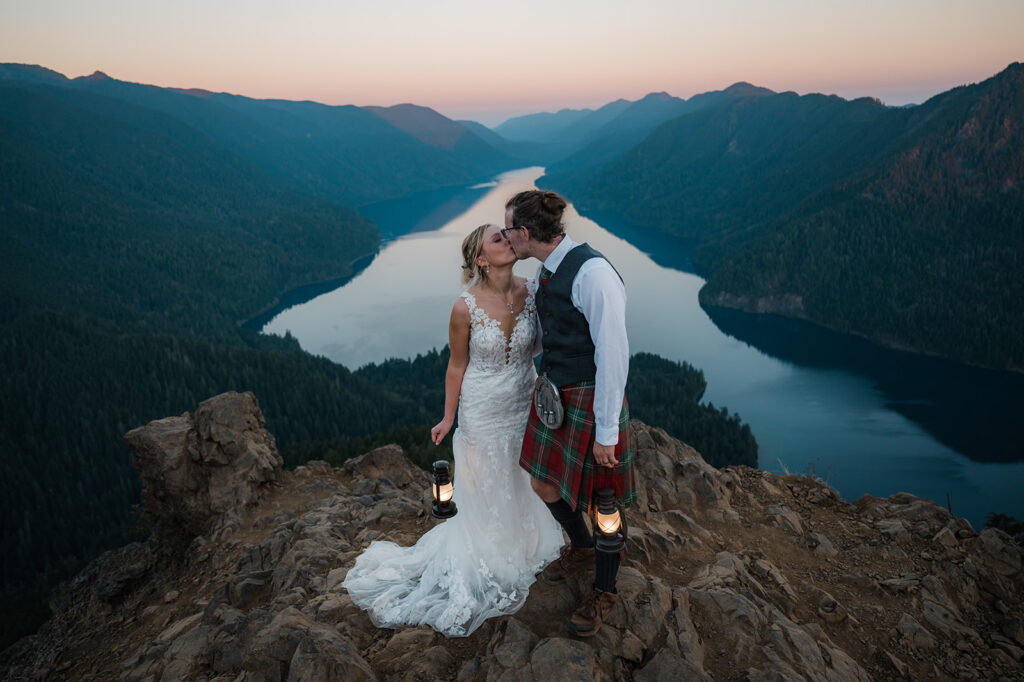 Bride and groom kiss while holding lanterns at the top of Mount Storm King