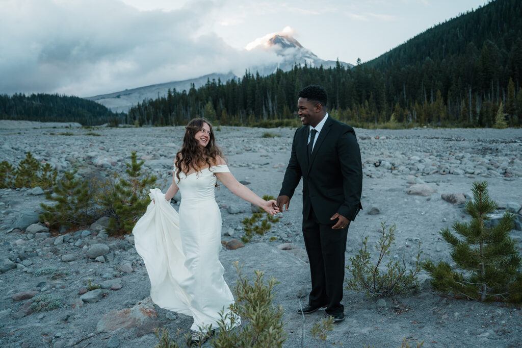 Bride and groom take couples portraits with Mt. Hood peaking through the clouds in the backdrop