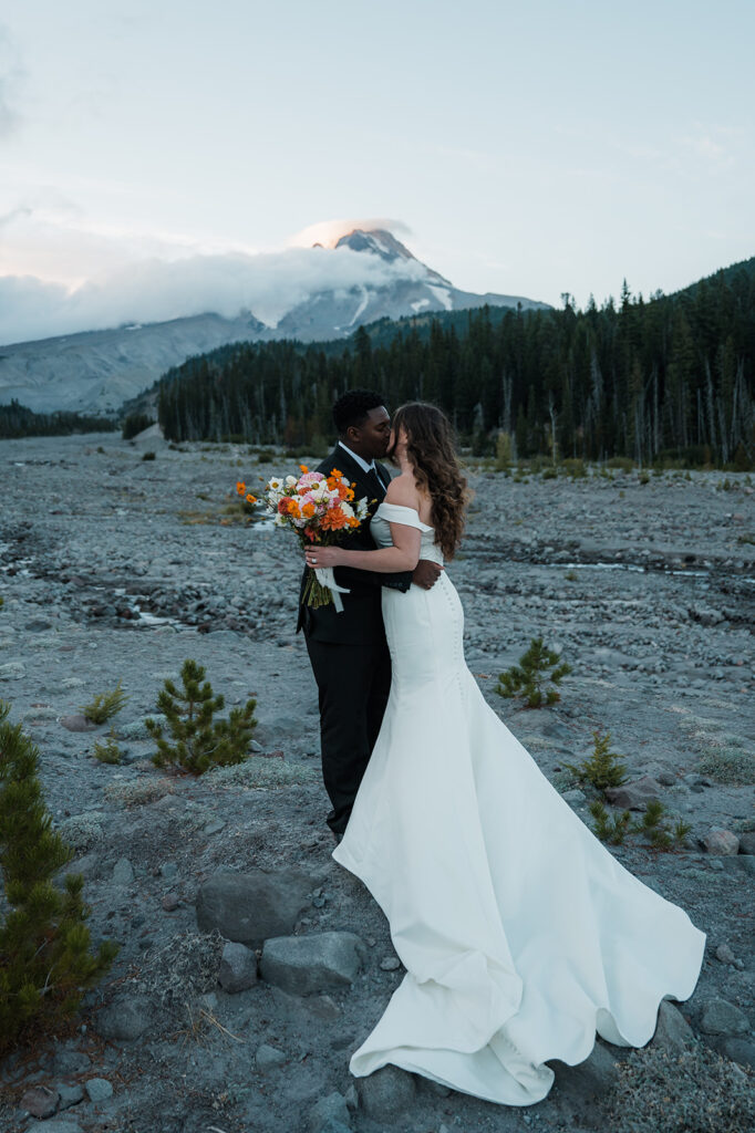 Bride and groom take couples portraits with Mt. Hood peaking through the clouds in the backdrop