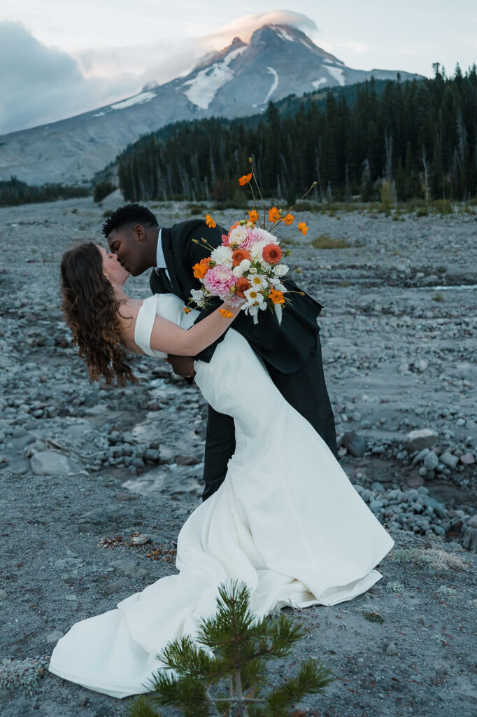 Bride and groom take couples portraits with Mt. Hood peaking through the clouds in the backdrop