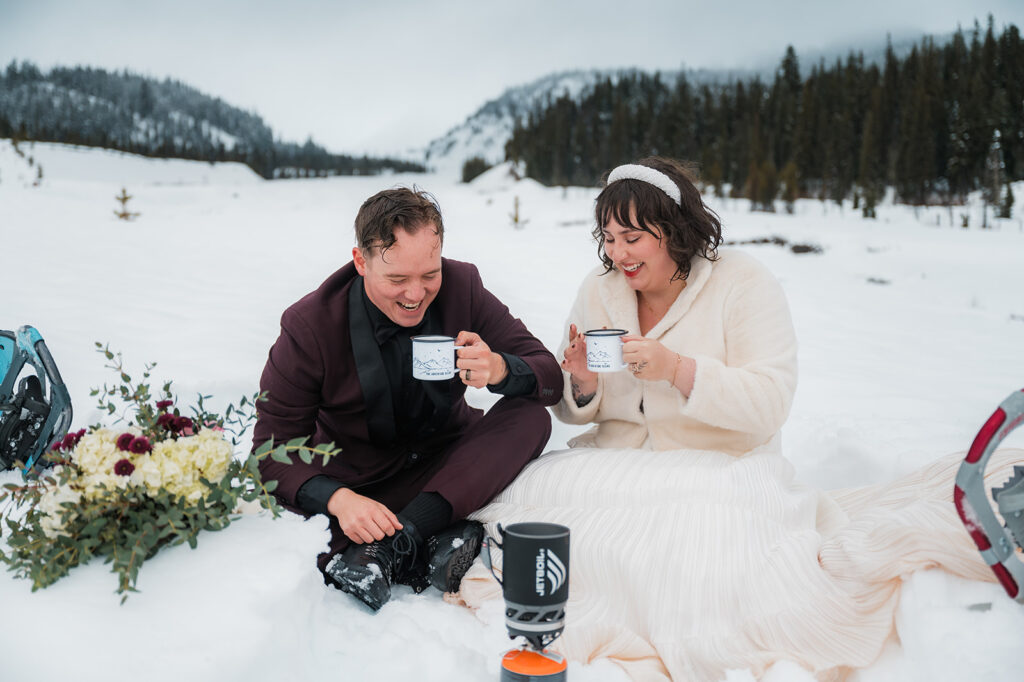 newly married couple laughing and drinking hot cocoa after saying their vows during their winter elopement day at Mount Hood Oregon