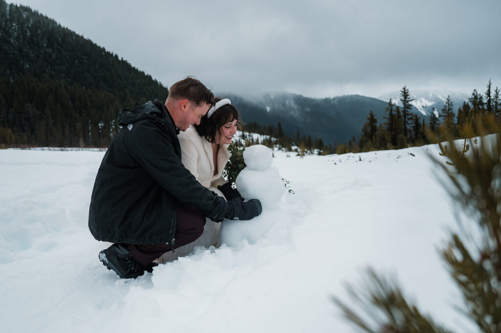 couple building a snowman during their winter elopement day in Oregon