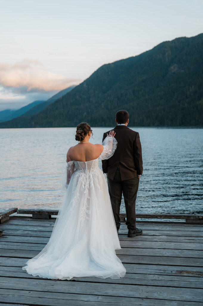 Bride and groom sharing a first look on the dock at Lake Crescent during sunrise, with calm water reflecting the golden sky