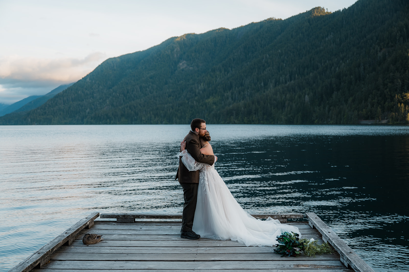 Bride and groom sharing a first look on the dock at Lake Crescent during sunrise, with calm water reflecting the golden sky