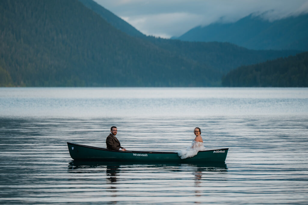 Bride and groom paddling a canoe on Lake Crescent, smiling and enjoying the peaceful morning water