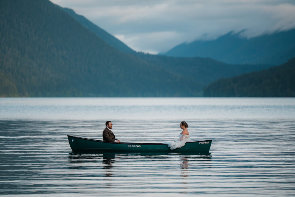 Bride and groom paddling a canoe on Lake Crescent, smiling and enjoying the peaceful morning water