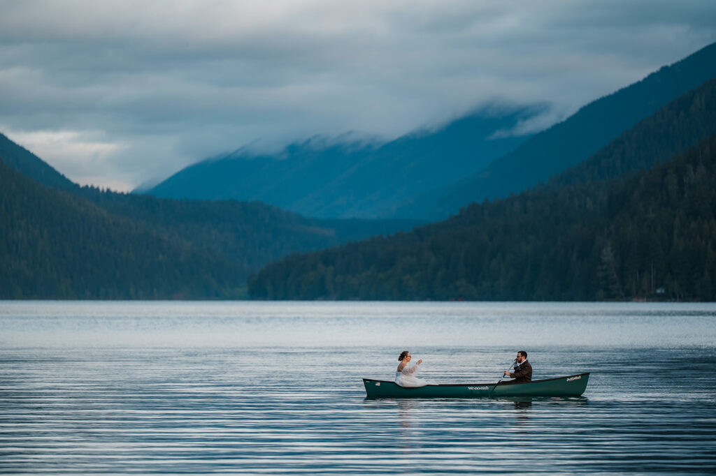 Bride and groom paddling a canoe on Lake Crescent, smiling and enjoying the peaceful morning water