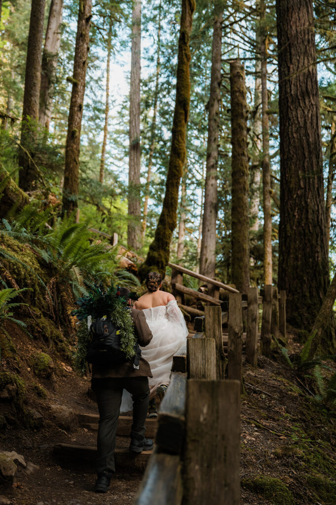 Bride and groom walking hand-in-hand on a forest trail to Marymere Falls, surrounded by mossy trees