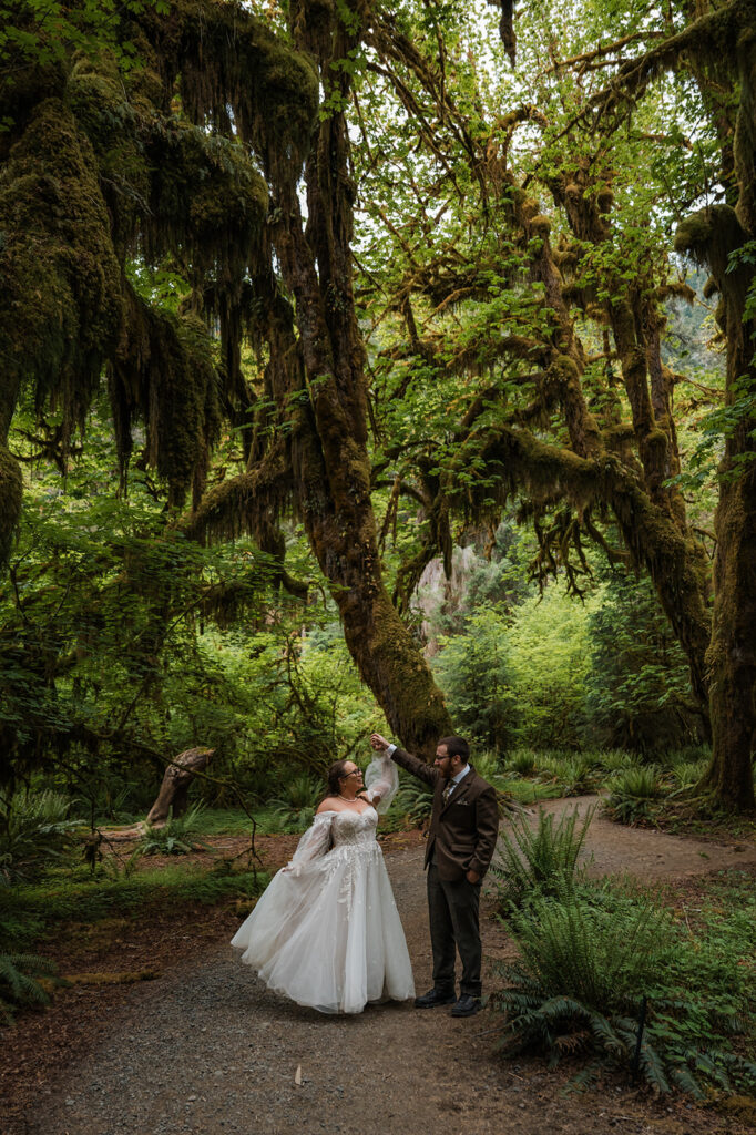 Bride and groom walking through the moss-covered Hoh Rainforest, with sunlight filtering through tall trees