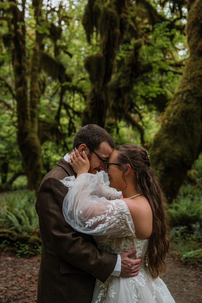 Bride and groom embracing in the Hoh Rainforest, surrounded by ancient trees draped in green moss