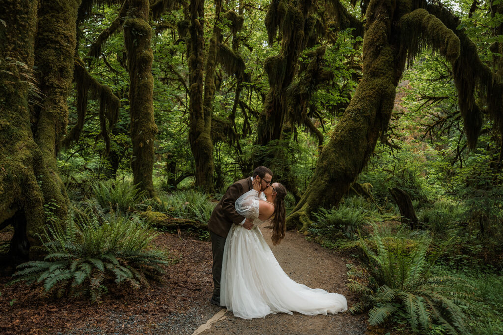 Bride and groom embracing in the Hoh Rainforest, surrounded by ancient trees draped in green moss