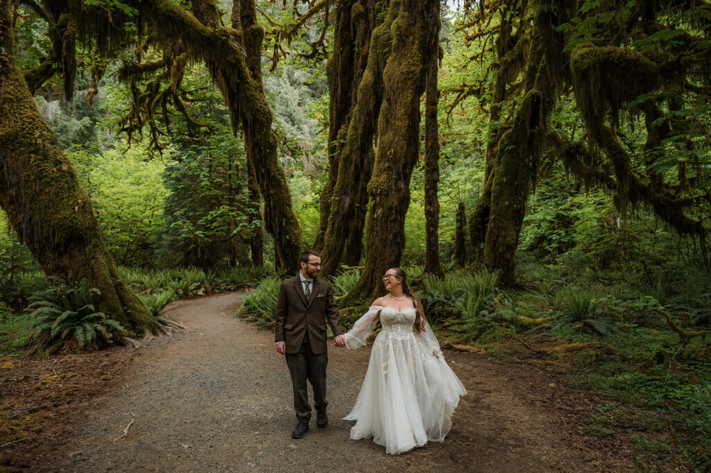 Bride and groom walking through the moss-covered Hoh Rainforest, with sunlight filtering through tall trees