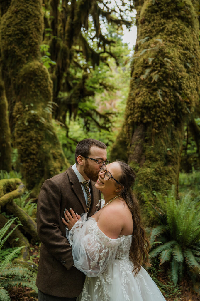 Bride and groom embracing in the Hoh Rainforest, surrounded by ancient trees draped in green moss