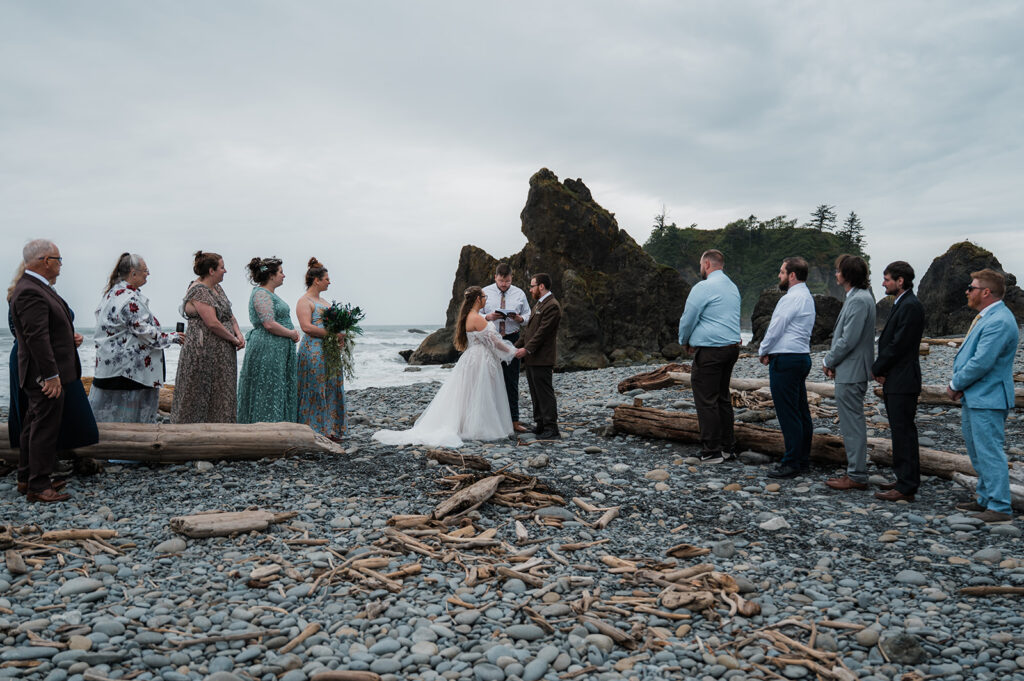 Bride and groom exchanging vows at sunset on Ruby Beach, with their closest family members nearby and sea stacks in the background