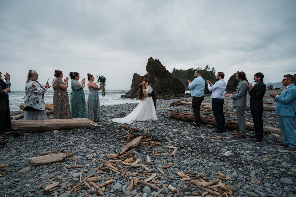 Bride and groom exchanging vows at sunset on Ruby Beach, with their closest family members nearby and sea stacks in the background