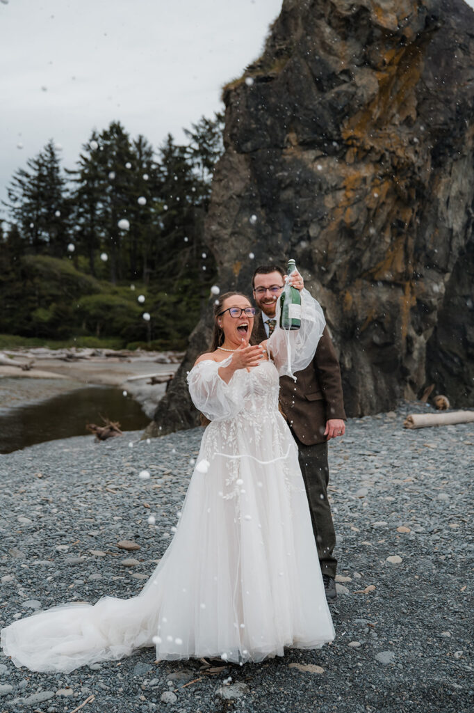 Bride and groom popping champagne on Ruby Beach to celebrate their elopement day