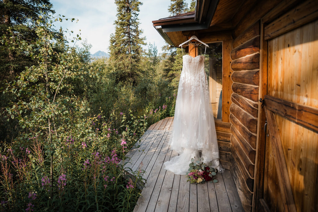 bridal gown hanging up outside a cabin in alaska surrounded by fireweed